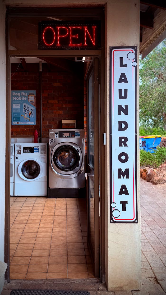 Entrance of a laundromat with neon open sign and washing machines visible.